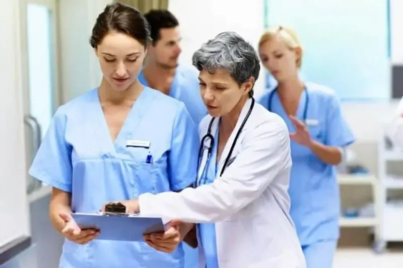 A group of nurses are standing around and looking at something.